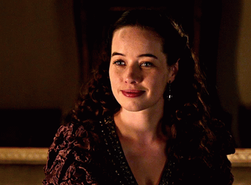A Woman With Curly Hair Is Smiling And Wearing A Purple Dress GIF