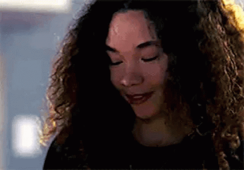 a woman with curly hair is smiling with her eyes closed and looking down .