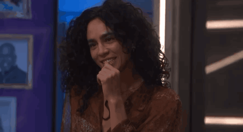 a woman with curly hair is smiling with her hand to her mouth
