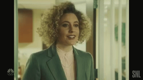 a woman with curly hair is standing in a doorway wearing a green suit and a pink shirt .