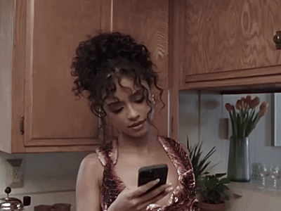 A Woman With Curly Hair Is Using A Cell Phone GIF