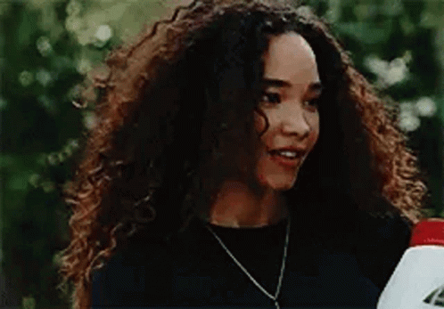 a woman with curly hair is wearing a black shirt and a necklace and holding a bottle .