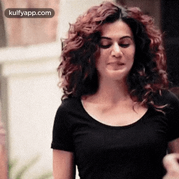 A Woman With Curly Hair Is Wearing A Black T-Shirt And Making A Funny Face . GIF