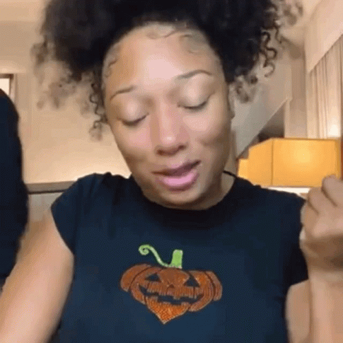 A Woman With Curly Hair Is Wearing A Black T-Shirt With A Pumpkin On It And Her Eyes Closed . GIF