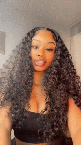 A Woman With Curly Hair Is Wearing A Black Top And A Necklace GIF