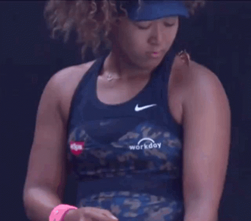 A Woman With Curly Hair Is Wearing A Blue Tank Top And A Hat . GIF