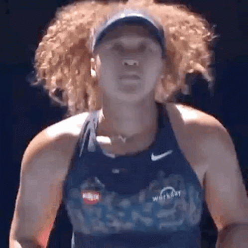 A Woman With Curly Hair Is Wearing A Blue Tank Top And A Hat While Playing Tennis . GIF