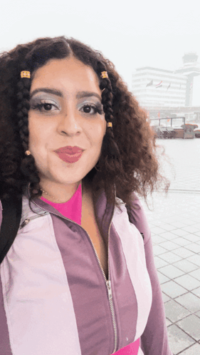 a woman with curly hair is wearing a purple and white striped jacket