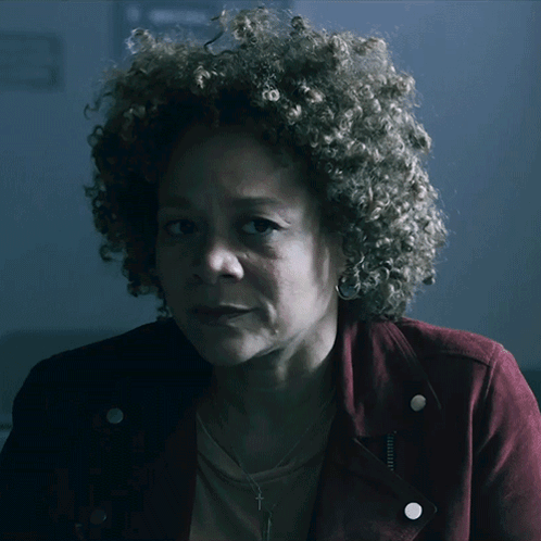 A Woman With Curly Hair Is Wearing A Red Jacket And Earrings GIF