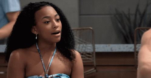 A Woman With Curly Hair Is Wearing A Strapless Top And Earrings GIF