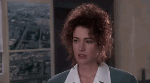 A Woman With Curly Hair Is Wearing A Suit And A White Shirt And Making A Funny Face . GIF