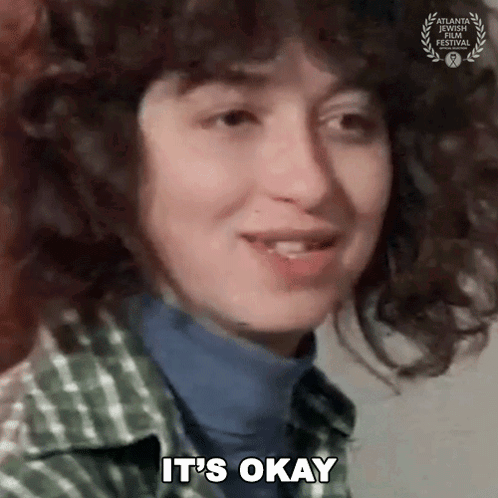 Curly Haired Woman Saying It's Okay In Plaid Shirt GIF