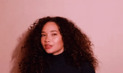 A Woman With Curly Hair Wearing A Black Turtleneck Sweater GIF