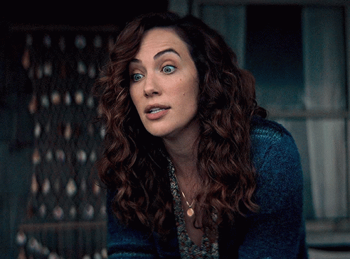 A Woman With Curly Hair Wearing A Blue Sweater And A Necklace GIF
