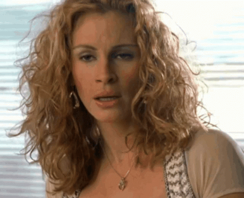 A Woman With Curly Hair Wearing A Necklace GIF