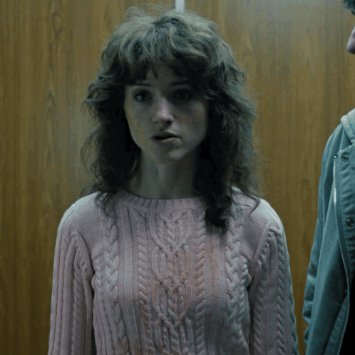 A Woman With Curly Hair Wearing A Pink Sweater Looks Surprised GIF
