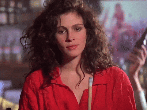 A Woman With Curly Hair Wearing A Red Shirt Holds A Pool Cue GIF