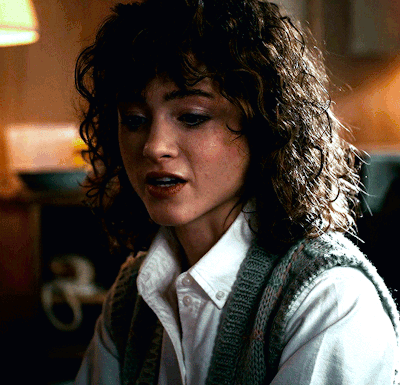 A Woman With Curly Hair Wearing A White Shirt And Sweater Vest GIF