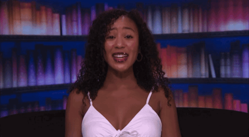 a woman with curly hair wearing a white tank top is smiling
