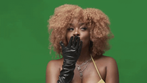 A Woman With Curly Hair Wearing A Yellow Top And Black Leather Gloves GIF