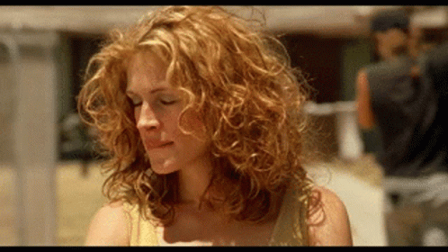 A Woman With Curly Red Hair Is Looking Down At Something . GIF