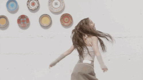 A Woman With Dreadlocks Is Dancing In Front Of Plates On A Wall GIF