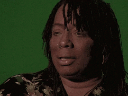 A Woman With Dreadlocks Is Making A Funny Face In Front Of A Green Screen GIF