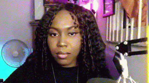 A Woman With Dreadlocks Is Sitting In Front Of A Microphone In A Room With A Fan . GIF