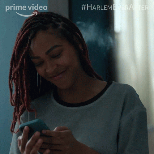 A Woman With Dreadlocks Is Smiling While Looking At Her Phone And The Words Prime Video Are Above Her GIF