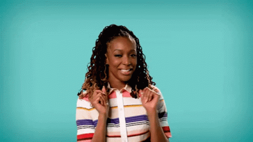 a woman with dreadlocks is wearing a colorful striped shirt and smiling with her hands on her shoulder .