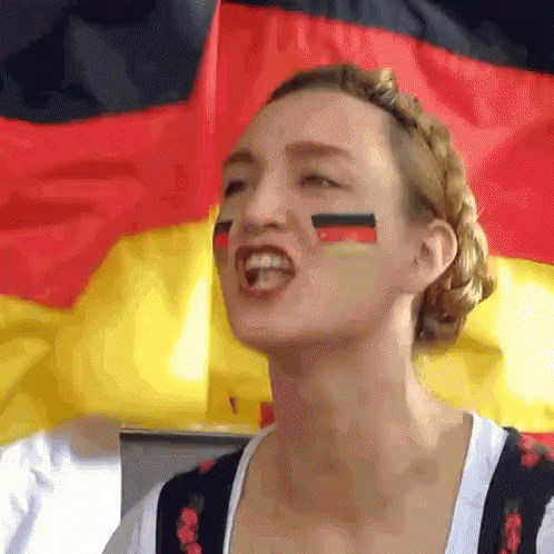 A Woman With Flags Painted On Her Face Stands In Front Of A German Flag GIF
