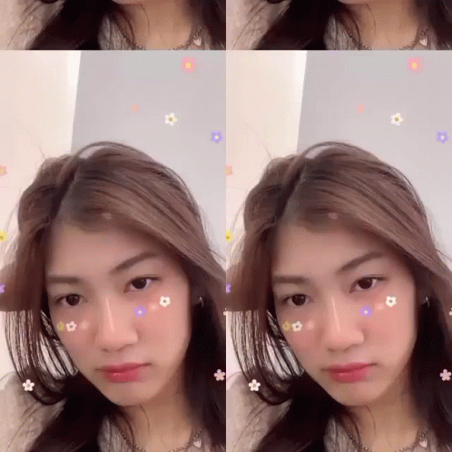 A Woman With Flowers On Her Face Is Looking At The Camera GIF