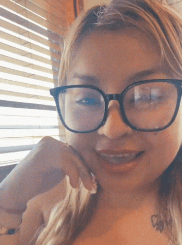 a woman with glasses and a tattoo on her chest smiles