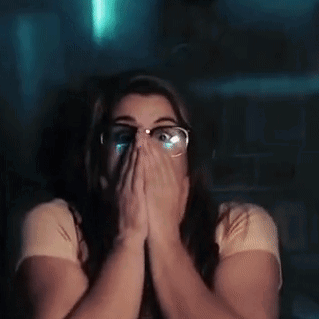 A Woman With Glasses Is Covering Her Face With Her Hands While Watching A Movie . GIF