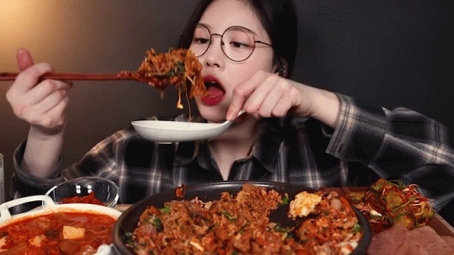 A Woman With Glasses Is Eating Food With Chopsticks GIF