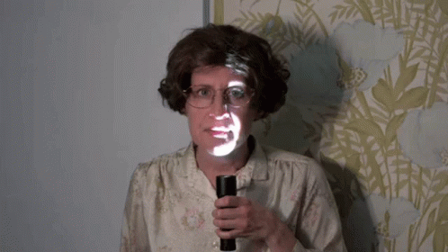 A Woman With Glasses Is Holding A Flashlight With A Face Projected On It GIF