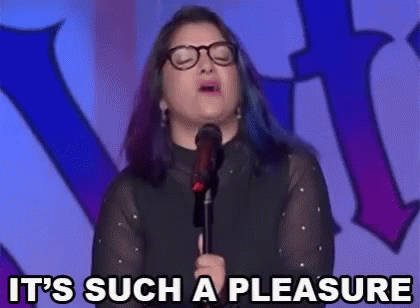 a woman with glasses is standing in front of a microphone and saying it 's such a pleasure .