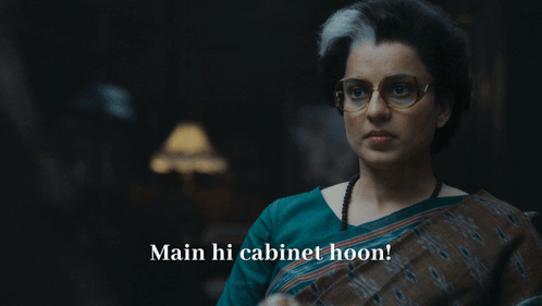 A Woman With Glasses Says Main Hi Cabinet Hoon In A Dark Room GIF