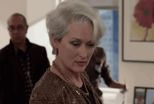A Woman With Gray Hair And A Necklace Looks Down GIF