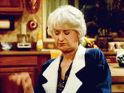 A Woman With Gray Hair Is Sitting In A Kitchen Making A Funny Face GIF