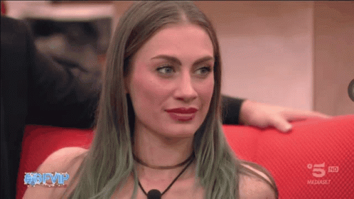 A Woman With Green Hair Is Sitting On A Red Couch In Front Of A 5 Hd Sign GIF