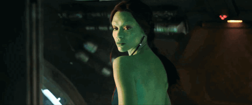 A Woman With Green Hair Is Standing In Front Of A Window GIF