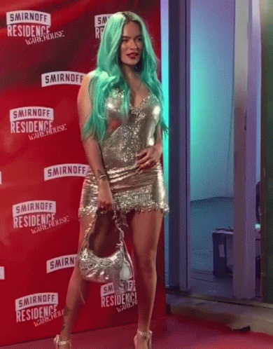 A Woman With Green Hair Is Standing On A Red Carpet In Front Of A Smirnoff Sign GIF