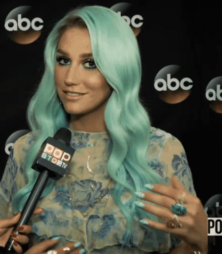 A Woman With Green Hair Is Talking Into A Microphone That Says Pop Story GIF