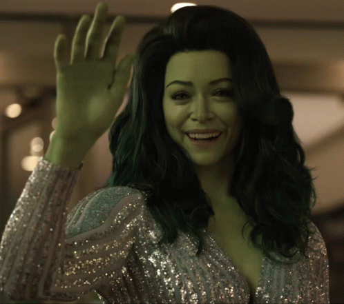 A Woman With Green Hair Is Waving Her Hand And Smiling GIF
