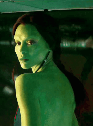 A Woman With Green Skin Is Looking Over Her Shoulder At The Camera GIF
