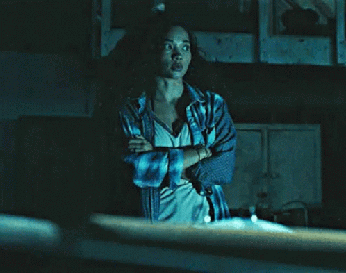 a woman with her arms crossed is standing in a dark room .