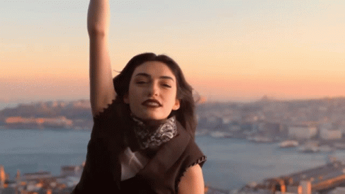 A Woman With Her Arms In The Air Looks At The Camera With A City In The Background GIF