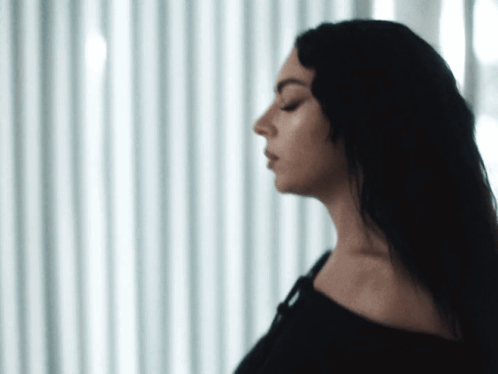 A Woman With Her Eyes Closed Is Standing In Front Of A Window GIF