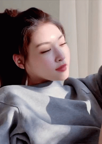 A Woman With Her Eyes Closed Is Wearing A Grey Sweater GIF